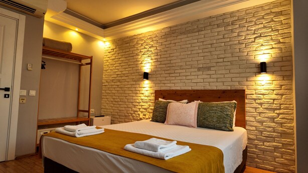 A hotel room with a brick wall, a wooden headboard, and two wall-mounted lights. - Hotel Zurich Oldtown (Antalya)