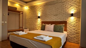 A hotel room with a brick-patterned wall, a wooden headboard, and a bed with white linens and a mustard-colored throw. - Hotel Zurich Oldtown (Antalya)