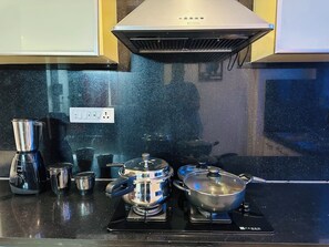 A kitchen with a stove, pots, a coffee maker, and a range hood. - 2-bedroom apartment in a high end residential location in Bengaluru city Centre. (Bengaluru)