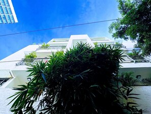 Un edificio moderno con fachada blanca, varios balcones y abundante vegetación en primer plano.