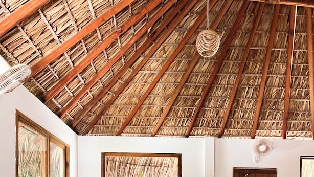 A cozy room with a thatched roof, a large window, a sofa with red cushions, and a small wooden table. - Casa Leone La Punta (Brisas de Zicatela)