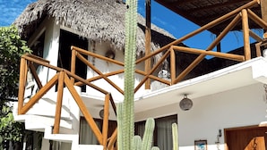 A white building with a wooden balcony, a thatched roof, and a cactus in the foreground. - Casa Leone La Punta (Brisas de Zicatela)