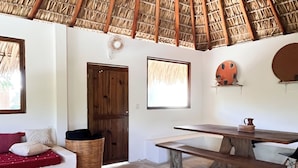 Um interior rústico com um telhado de palha, um banco de madeira, uma mesa de jantar e um tabuleiro de xadrez.
