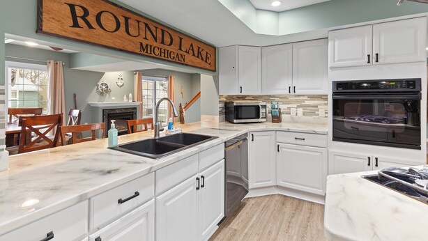 A modern kitchen with white cabinetry, a large wooden sign above the sink, and a view of the outside.