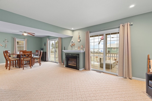 A spacious living room with a fireplace, a dining area with wooden furniture, and large sliding glass doors leading to a deck.