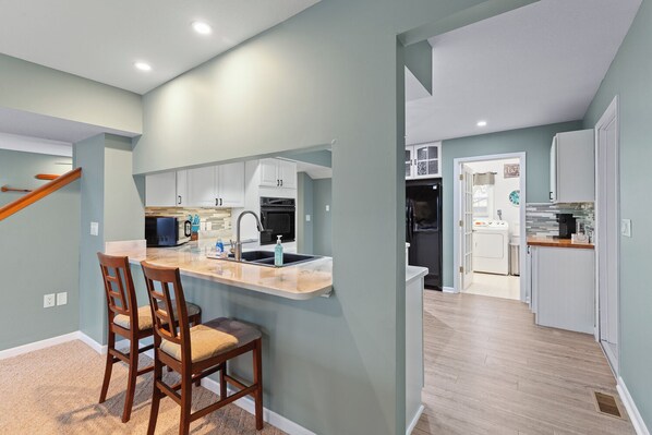 A modern kitchen with a central island, wooden chairs, and a built-in oven.
