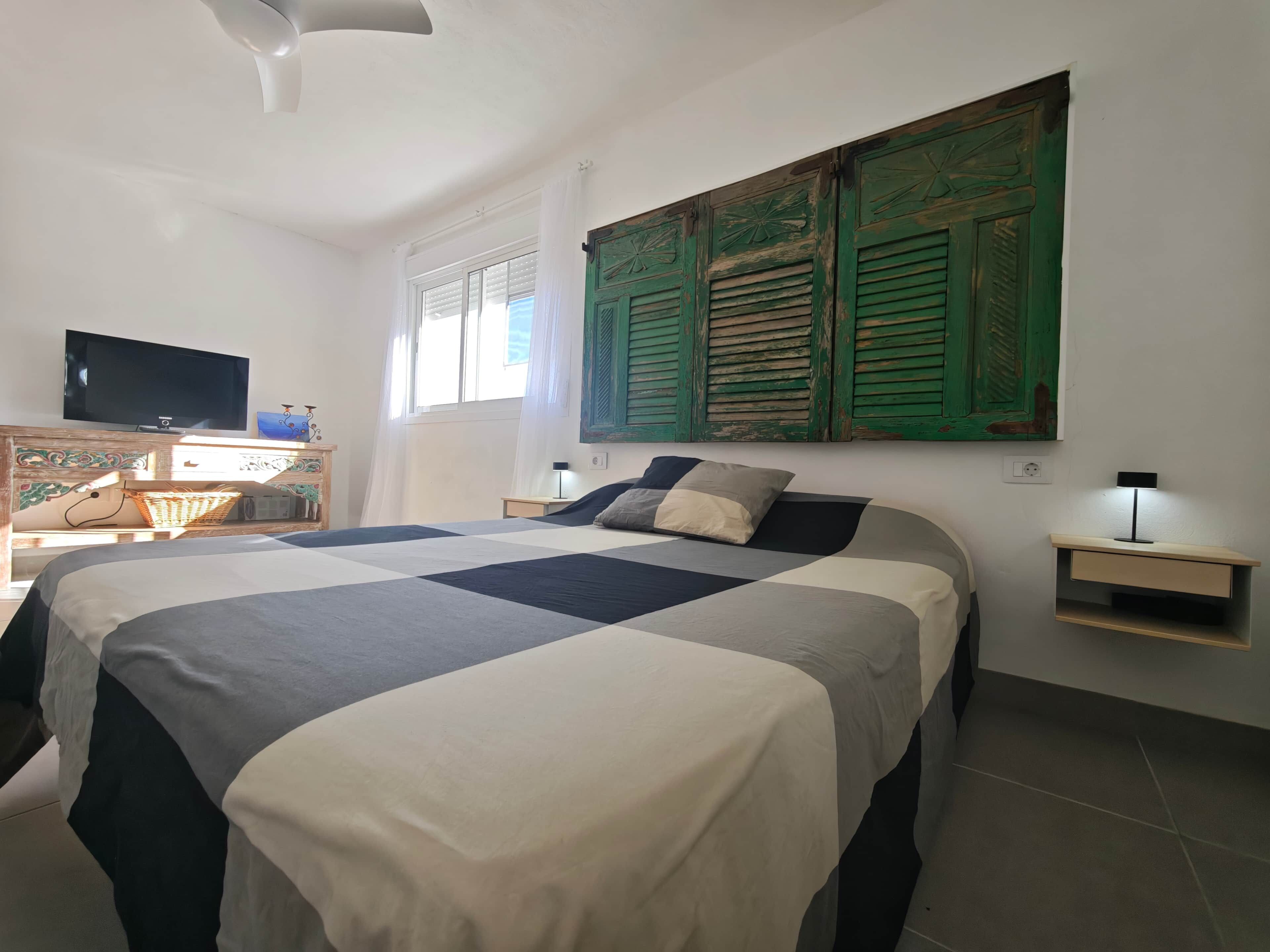 A bedroom with a bed, a television, a nightstand, and a wall-mounted shelf.