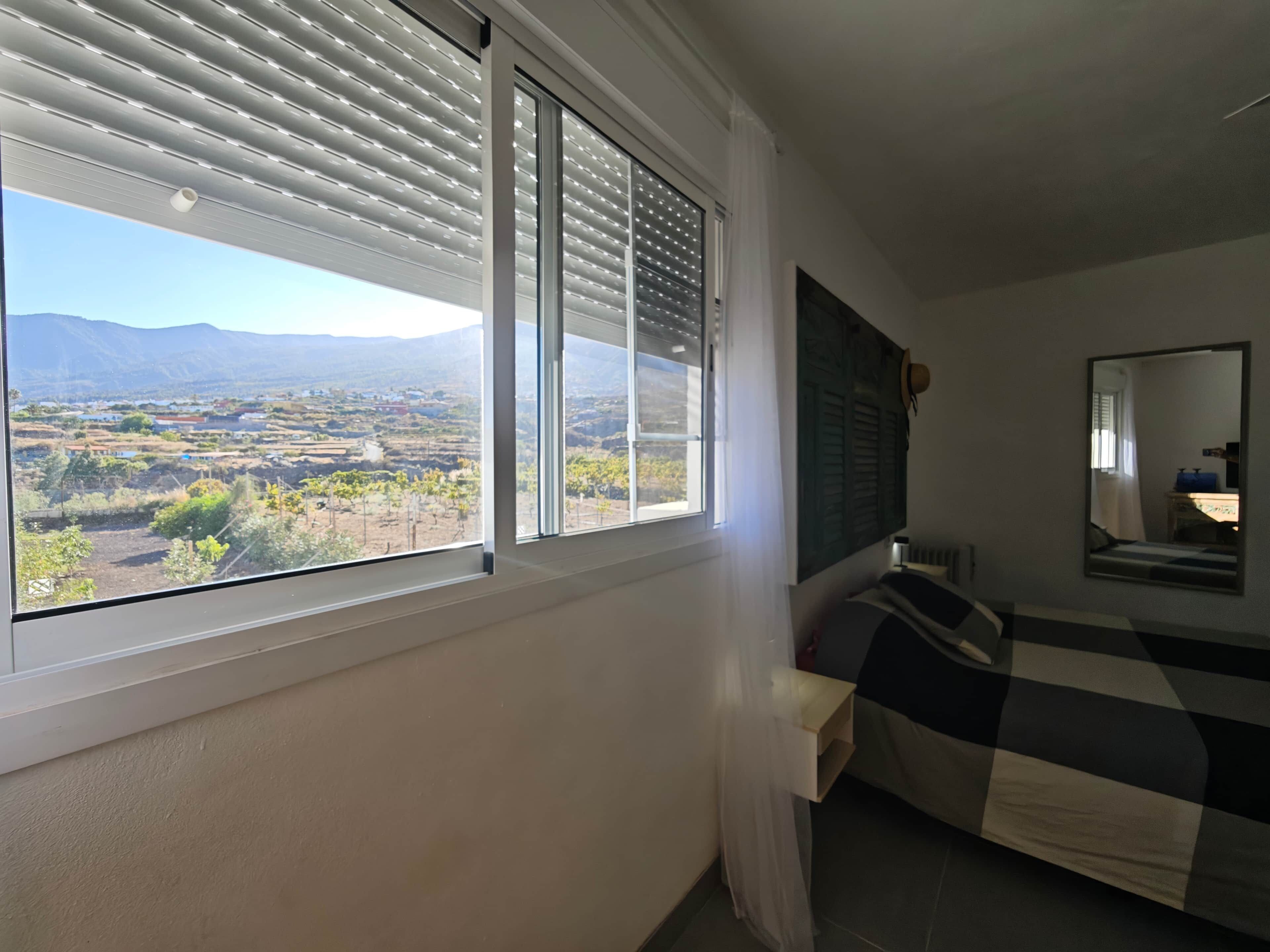 Une chambre avec une grande fenêtre, un lit, un miroir et une vue sur un paysage montagneux.