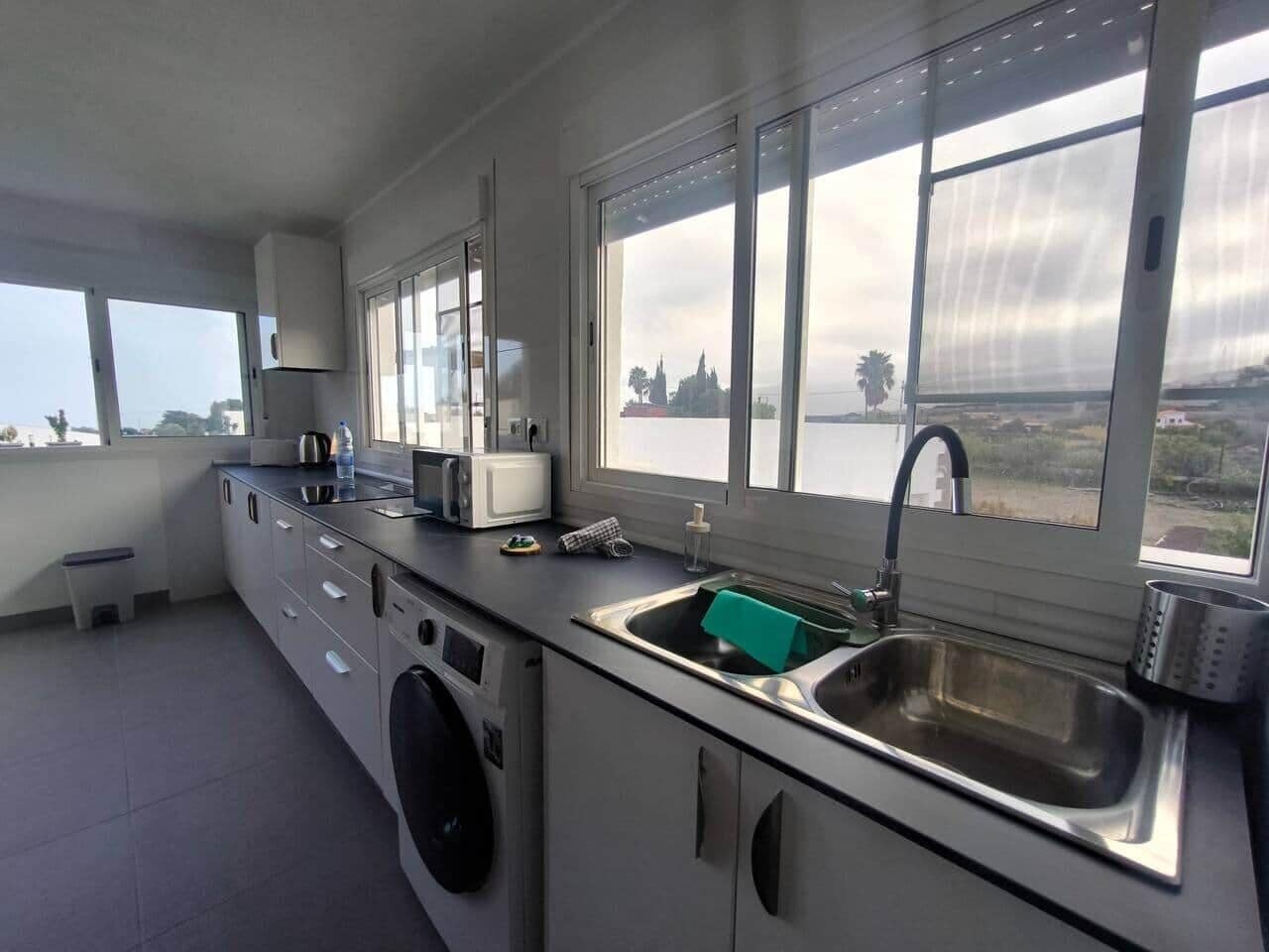 A compact kitchen with a washing machine, a sink, and a window overlooking a landscape.