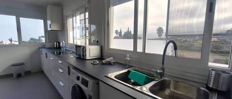 A compact kitchen with a washing machine, a sink, and a window overlooking a landscape.