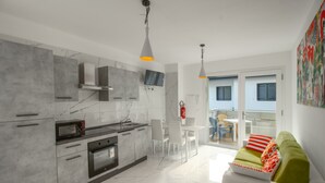 A modern kitchen with marble countertops, a built-in oven, and a dining area with a white table and chairs. - Modern flat with shared pool (Bibione)