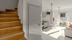 A modern interior with a wooden staircase, a kitchen with white cabinets, and a dining area with a white table and chairs. - Modern flat with shared pool (Bibione)