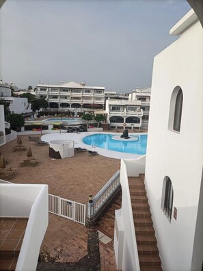 Zona de piscina con una piscina circular, sillones de descanso y una escalera que lleva a un edificio.