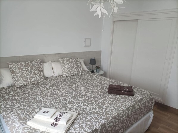 Una cama bien hecha con una colcha estampada y almohadas, una mesita de noche con una lámpara y una pequeña planta en maceta.