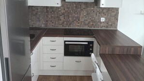 A compact kitchen with white cabinets, a built-in oven, a stainless steel refrigerator, and a patterned backsplash. - The Balcony of the 4 Moons - Apartment 631 (Costa Teguise)