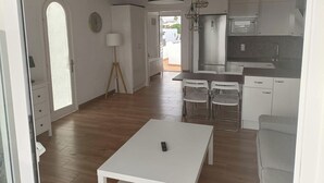 A modern kitchen with white cabinets, a stainless steel refrigerator, and a dining area with a white table and chairs. - The Balcony of the 4 Moons - Apartment 631 (Costa Teguise)