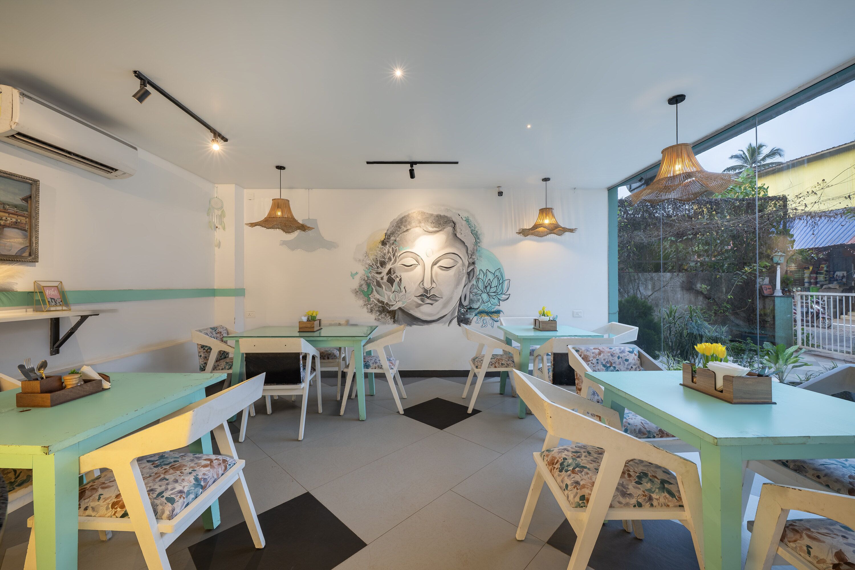 A dining area with teal tables and white chairs, a large mural on the wall, and pendant lighting.