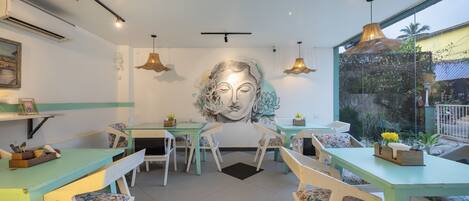 A dining area with teal tables and white chairs, a large mural on the wall, and pendant lighting.