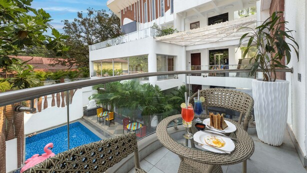 Un área de piscina en la azotea con barandilla de vidrio, muebles de mimbre y una mesa de comedor con una bebida y un postre.