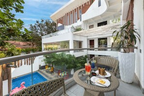Un área de piscina en la azotea con barandilla de vidrio, muebles de mimbre y una mesa de comedor con una bebida y un postre.