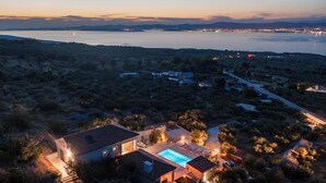 En vy över en fastighet, tagen från luften, som visar en pool, ett stort hus och utsikt över havet.