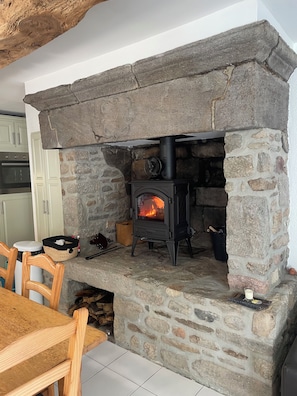 Una chimenea de piedra con un horno de leña negro, un ventilador y un vaso de leche sobre el hogar.