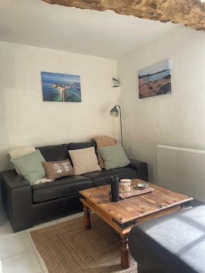 Un salon avec un canapé en cuir noir, une table basse en bois et deux tableaux accrochés au mur.
