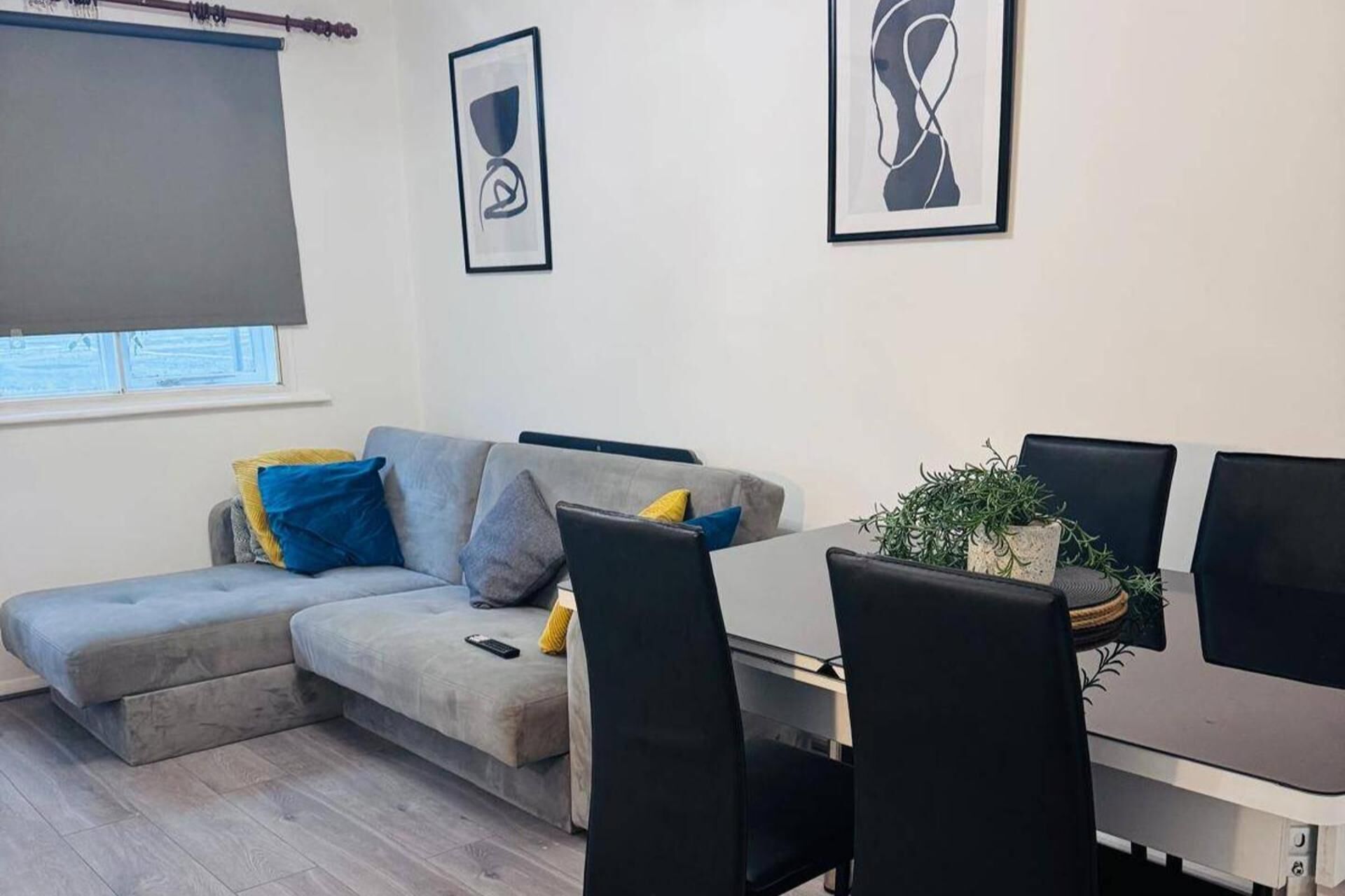 A modern living room with a grey sectional sofa, a dining table with chairs, and two framed artworks on the wall.