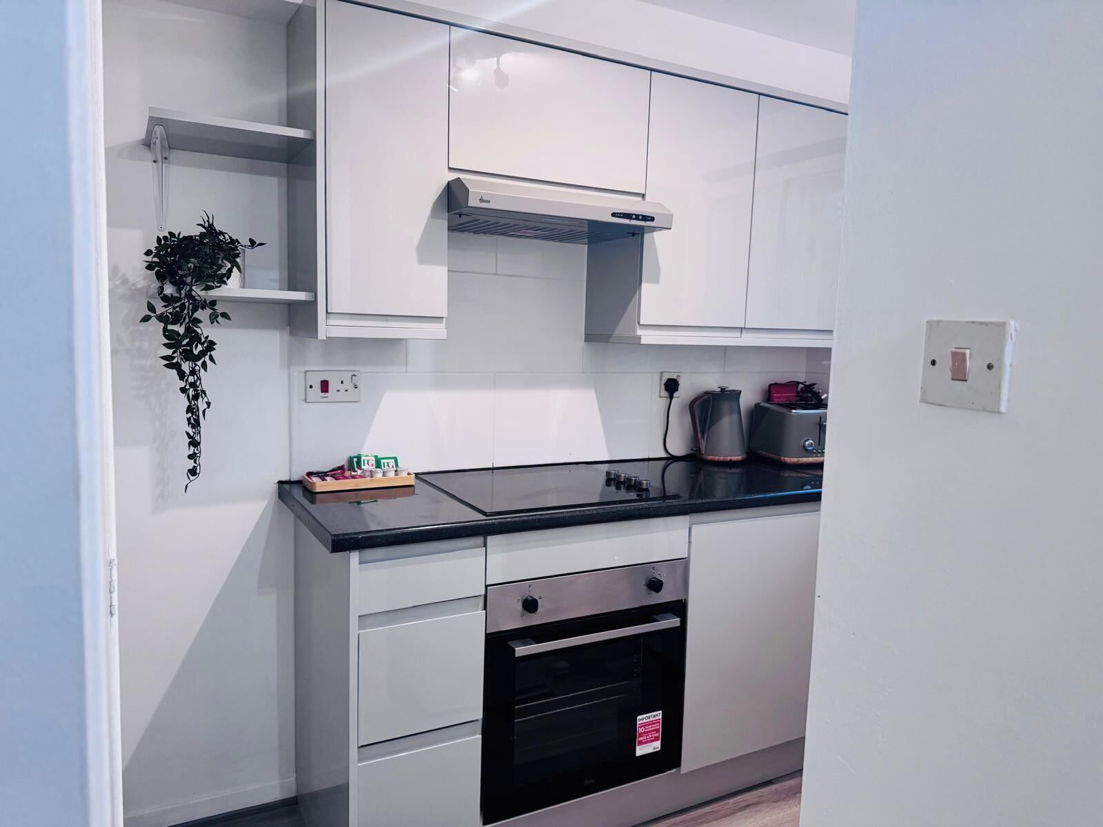Eine moderne Küche mit weißen Schränken, einer schwarzen Arbeitsplatte, einem Backofen und einer Kaffeemaschine.