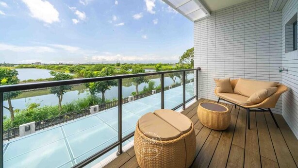 A balcony with a view of a lake and greenery, a wicker sofa, and a round wicker stool. - Xiuhu Lodge (Jiaoxi)