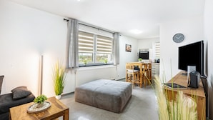 Ein modernes Wohnzimmer mit einer Couch, Hocker, einem Holztisch und einer Küchenzeile mit Esstisch und Stühlen.