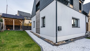 Ein modernes, zweistöckiges Haus mit weißer Fassade, einer überdachten Garage und einer Auffahrt mit Kies.