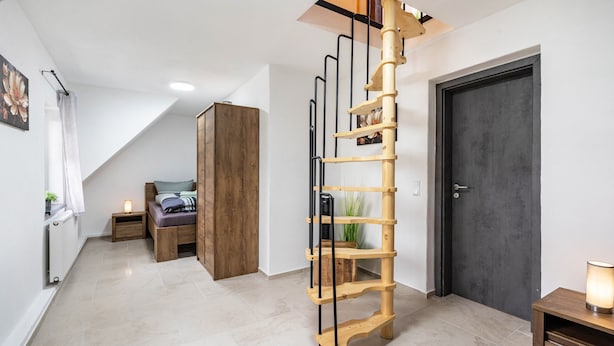 Ein modernes Interieur mit einer leiterartigen Holzkonstruktion, einer dunklen Tür und einem Bett mit Kopfteil.