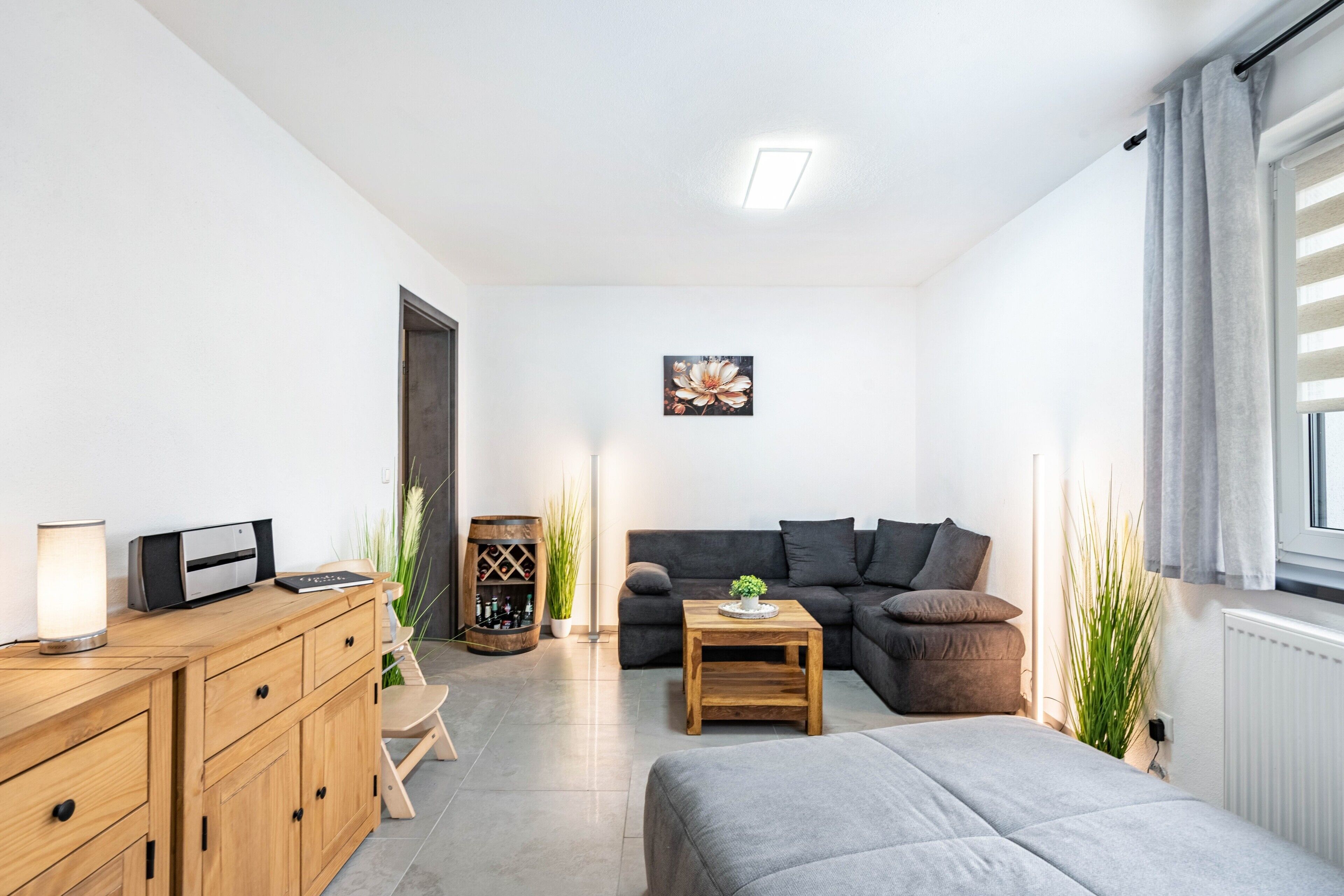 Ein modernes Wohnzimmer mit einer Couch, einem kleinen Tisch, einem Schrank, einer Heizung und einem Fenster mit Vorhängen.