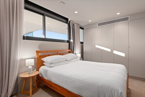 A neatly made bed with white linens, a wooden headboard, and a bedside table with a lamp. - Modern 1-bed With Tamarama Beach Views (Sydney)