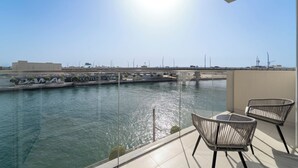 A balcony with two wicker chairs, a glass railing, and a view of a river with a bridge and buildings in the background. - 2BR M Room CF7 B Partial Canal View (Dubai)