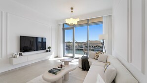 A modern living room with a large TV, a sofa, a coffee table, and a view of the harbor. - 2BR M Room CF7 B Partial Canal View (Dubai)