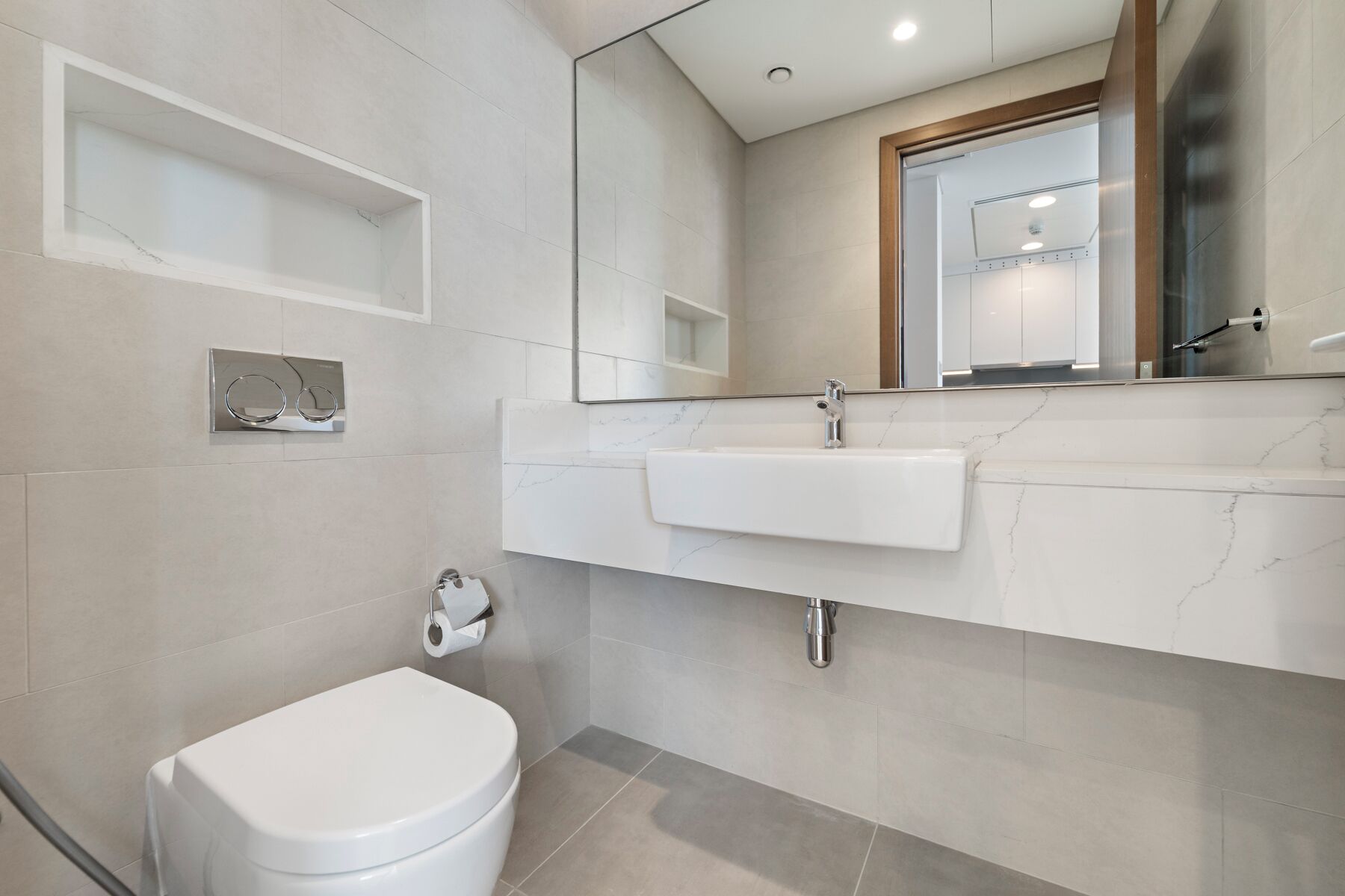 Un baño moderno con un inodoro blanco, un lavabo con espejo y un perchero para toallas.