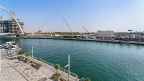 A waterfront promenade with a marina, construction cranes, and a modern building under construction. - 2BR M Room CF7 B Partial Canal View (Dubai)