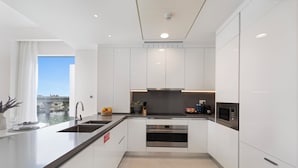 A modern kitchen with white cabinetry, a stainless steel sink, and an oven. - 2BR M Room CF7 B Partial Canal View (Dubai)
