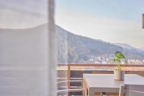 A balcony with a potted plant, a table, and a view of a town and mountains. - Bärbel, Black Forest style (Baiersbronn)