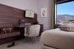Hotelkamer met een bed, een bureau met een laptop, een stoel, een handtas, wijnglazen en een lijst aan de muur.