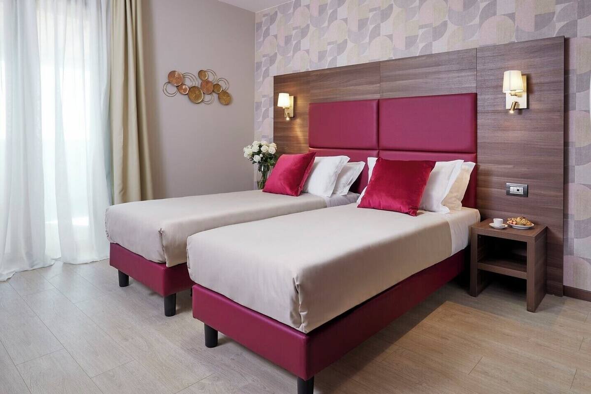 A hotel room with two beds, a nightstand, a wall-mounted lamp, and a decorative wall piece.