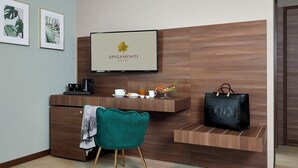 A hotel reception area with a wooden reception desk, a television displaying the hotel name, a green chair, and a black handbag on the counter. - HOTEL SPIGAMONTI (Negrar)