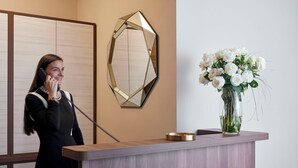 A reception desk with a vase of white flowers, a geometric mirror, and a telephone. - HOTEL SPIGAMONTI (Negrar)