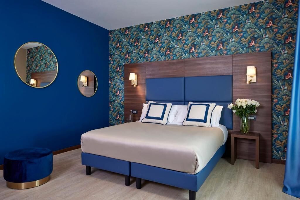 Un dormitorio con una cama grande, dos mesitas de noche, un espejo y una pared con estampado floral.