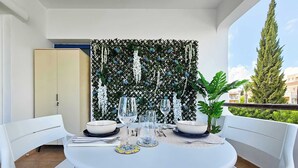 A dining area with a round table, white chairs, and a decorative wall with hanging plants. - Stylish 1BR Apt. Pool Views | Private Patio | 1min walk to 5-star Gym (Pafos)