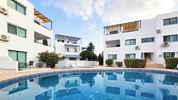 A modern residential building with a swimming pool, outdoor seating, and a covered patio area. - Stylish 1BR Apt. Pool Views | Private Patio | 1min walk to 5-star Gym (Pafos)