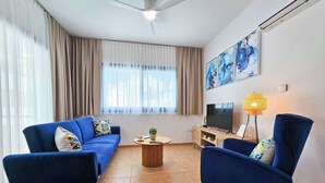 A living room with a blue sofa, a matching armchair, a coffee table, a TV, and a lamp. - Stylish 1BR Apt. Pool Views | Private Patio | 1min walk to 5-star Gym (Pafos)