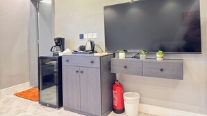 Una habitación moderna con puerta de cristal, una pequeña kitchenette, un televisor de pantalla plana montado en la pared y un extintor en el suelo.